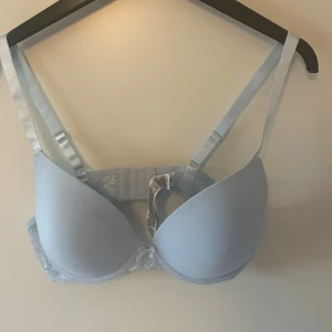 Ljusblå bh från Censored 85D - Säljer en ljusblå bh från Censored i storlek 85D. Bh:n har vadderade kupor, justerbara axelband och spetsdetaljer på sidorna. Söt liten rosett framtill och klassisk hakknäppning bak. Perfekt för dig som gillar en enkel men ändå söt look.