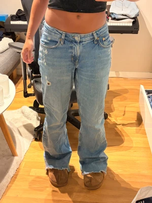 lågmidjade ljusblå jeans - storlek 40. låg midja, breda ben med bootcut och slitna detaljer. 