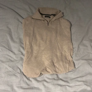 Beige half zip tröja Jack & Jones - Snygg beige långärmad tröja från Jack & Jones med half zip och hög krage. Tröjan är stickad i mjukt material och har ribbade muddar vid ärmslut och nederkant. Perfekt för dig som gillar enkel och clean stil.
