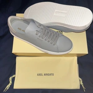 Grå sneakers från Axel Arigato - Helt nya och oanvända ”Clean 90 sneaker Light Grey, Axel arigato” (nypris ~2950kr) . Skorna har ovandel i slätt skinn, grå snörning och vit platt sula. Baktill finns en detalj i ljus mocka. Perfekta för dig som gillar stilrena och eleganta sneakers. Ställ gärna frågor om du har några:)