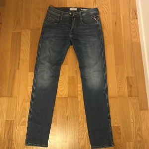 Replay Anbass Hyperflex jeans blå - Snygga Replay Anbass Hyperflex jeans i mörkblå tvätt med slim fit. Klassisk femficksmodell, dragkedja och knapp framtill. Stretchigt material för extra komfort och cool faded effekt på låren. Perfekt passform och stilren look.