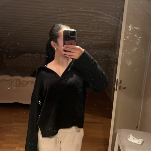 Svart stickad tröja från AWARE - Svart stickad tröja från AWARE med v-ringad krage och långa ärmar. Tröjan har en loose passform och är tillverkad i ett mjukt stickat material. Perfekt för lager-på-lager och chill dagar.