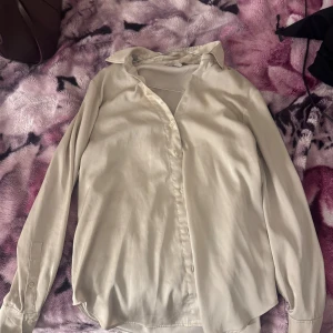 Beige långärmad skjorta med knappar - Stilren beige skjorta med klassisk krage och knäppning framtill. Skjortan har långa ärmar med manschett och är tillverkad i ett mjukt, lätt material som ger en avslappnad men ändå snygg look.