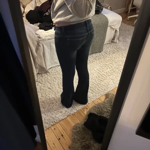 Mörkblå bootcut jeans med slitning - Snygga mörkblå jeans med bootcut passform och låg midja. Jeansen har markerade sömmar, slitning på ena knät och  fickor fram och bak. Materialet är stretchigt denim som sitter skönt. 