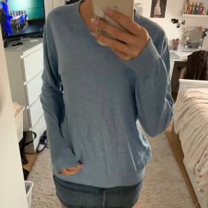 Ljusblå v-ringad stickad tröja - Ljusblå stickad tröja med v-ringning och långa ärmar. Tröjan har ribbade muddar vid ärmslut och nederkant, vilket ger en snygg och enkel look. Perfekt att matcha med jeans eller kjol för en chill stil.