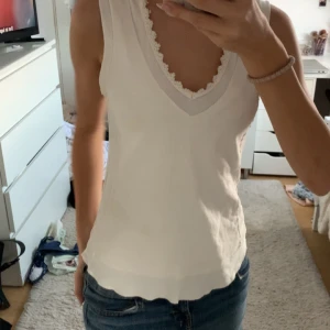 Vit ärmlös linnetopp med spets - Säljer en söt vit linnetopp med v-ringning och spetsdetalj längs urringningen. Toppen är ärmlös och har en lätt, luftig känsla som passar perfekt till jeans eller kjol. Enkel och stilren design som är lätt att matcha.