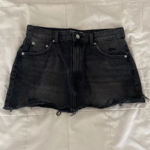 Svarta jeanskjol från Pull&Bear - Snygg svart jeanskjol från Pull&Bear i medium med råa, slitna kanter och klassisk femficksdesign. Kjolen har en mörk tvätt som ger en cool vibe. Perfekta för sommarens alla äventyr!