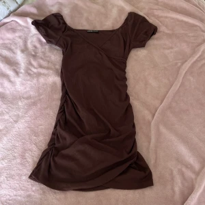 Brun ribbad kortklänning från SHEIN - Snygg brun kortklänning från SHEIN i ribbat material. Klänningen har puffiga korta ärmar, v-ringad hals och figurnära passform. Perfekt för dig som gillar en enkel men trendig look. Storlek M (EU 38).