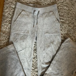 Grå mjukisbyxor från Juicy Couture - Snygga grå mjukisbyxor från Juicy Couture med dragsko i midjan och stora fickor fram. Byxorna har broderad logga på ena fickan och bakfickor med knapp. Skulle gissa att byxorna är xxs men passar både xs och s.