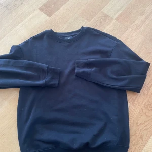 Svart sweatshirt från H&M Relaxed Fit - En svart sweatshirt från H&M i relaxed fit. Tröjan har rund halsringning, långa ärmar och ribbade muddar vid ärmslut och nederkant. Tillverkad i mjuk bomullsmix som är skön att bära. Perfekt för en chill och avslappnad stil. 