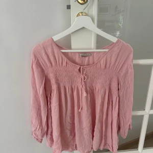 Rosa blus med knyt och smock - Söt ljusrosa blus från Rabalder som är köpt secondhand hos Erikshjälpen för 100kr. Har väldigt små vita färgfläckar, men det är inte något man lägger märke till.