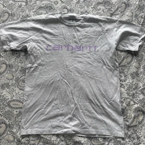 Grå Carhartt t-shirt med lila tryck - Snygg grå t-shirt från Carhartt med lila logga. Klassisk passform med rund hals och korta ärmar. Säjs då jag inte använder den längre.💕