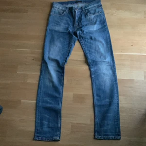 Blå Nudie Jeans (Tilted Tor) - Säljer ett par klassiska blå jeans från Nudie Jeans i rak modell. Jeansen är tillverkade av 100% ekologisk bomull och har snygga slitningar framtill. De har fem fickor, orangea sömmar och en stilren look som funkar till det mesta Storlek: W32 L34