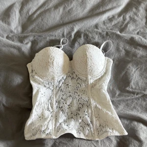 Vit spetskorsett med avtagbara axelband - Säljer en vit korsett med vacker spets och vadderade kupor. Toppen har avtagbara och justerbara axelband samt hakknäppning i ryggen. Figurnära passform och snygga sömmar framtill ger en riktigt clean och feminin look.
