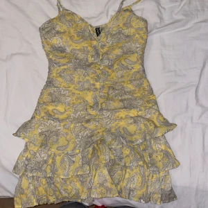 Gul mönstrad volangklänning H&M XS - Superfin gul kortklänning från H&M med paisleymönster i vitt och grått. Klänningen har smala axelband, volanger i kjolen och figurnära passform. Perfekt för dig som gillar färg och mönster! Sitter väldigt snatched 