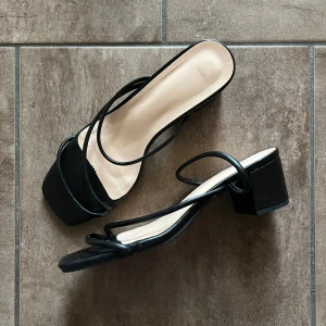 Svarta klackskor med tunna remmar - Svarta klackskor med fyrkantig tå, tunna remmar och låg blockklack. Snygg minimalistisk design med öppen tå och platt sula. Perfekta för sommarens alla outfits. Tillverkade i syntetmaterial. Storlek 39, normala i storleken. Klackhöjd 5cm.