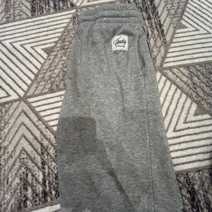 Grå mjukisbyxor från Frank Dandy - Grå mjukisbyxor från Frank Dandy med resår i midjan och sidofickor. Byxorna har en vit patch med Andy by Frank Dandy-logga framtill. Perfekta för chill dagar och riktigt sköna att ha på sig.