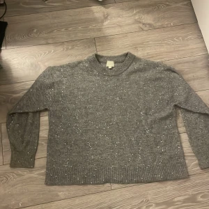 Grå glittrig stickad tröja H&M - Grå stickad tröja från H&M i storlek L med glittriga detaljer över hela tröjan. Klassisk rund halsringning och långa ärmar. Perfekt för dig som vill ha en mysig men ändå extra tröja med lite bling.