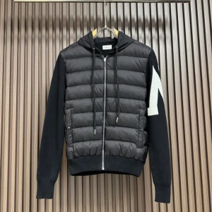 Svart pufferjacka med huva från Moncler - Svart pufferjacka från Moncler med huva och dragkedja framtill. Jackan har quiltad front i glansigt material, stickade ärmar med vit detalj och Moncler-logga på ena ärmen. Snygga snören i huvan och ribbade muddar ger en sportig vibe.