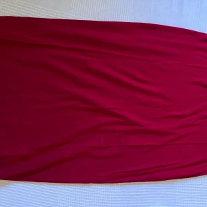 Röd långklänning  - En stilren röd långklänning från Indiska i mjukt och följsamt material. Klänningen har en enkel design utan mönster och är perfekt för dig som gillar en klassisk look med mycket färg.