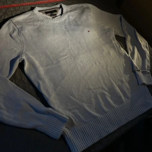 Ljusgrå stickad tröja Tommy Hilfiger XL/L - Snygg ljusgrå stickad tröja från Tommy Hilfiger i premium bomull. Klassisk modell med rund halsringning, ribbade muddar och diskret logga broderad på bröstet. Perfekt för dig som gillar stilrena och tidlösa plagg. Den funkar som både XL och L i storleken. Priset är inte fast så bara kom med förslag. Skickar inom 24 timmar