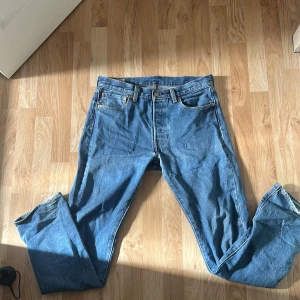 Levi's 501 blå jeans 32/34 - Klassiska blå Levi's 501 jeans med rak passform och knappgylf. Jeansen har fem fickor, tydliga sömmar och den ikoniska läderpatchen bak i midjan. Tillverkade i slitstarkt bomullsjeans, perfekt för en avslappnad och tidlös look.