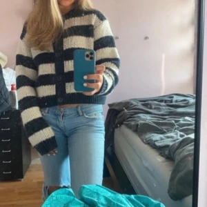 Randig stickad kofta i svart och vitt - Säljer en mysig stickad kofta med breda svarta och vita ränder. Koftan har stora knappar framtill, lång ärm och en lite croppad passform. Perfekt för att slänga över en t-shirt när det är kyligt ute. 
