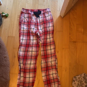 Röd-rutiga byxor från Kappahl 134/140 - Mysiga byxor från Kappahl i röd, vit och marinblå rutig bomull. De har resår i midjan och en stor marinblå rosett framtill. Perfekta för chill dagar hemma eller som pyjamasbyxor.
