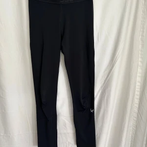 Svarta träningsleggings från SOC - Svarta leggings från SOC med tekniskt material som andas och håller dig torr. Tight passform och elastisk midja, perfekta för träning eller sport. Diskret logga på benet och smidigt tyg som ger bra rörelsefrihet.