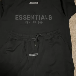 Svart Essentials Fear of God Set - Svart set från Essentials Fear of God med elastisk midja och snörning. Setet har en clean look med diskret logga framtill och är tillverkade i mjukt material för maximal komfort. Perfekta för en chill och stilren streetwear-outfit.