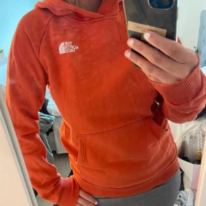 Orange hoodie från The North Face - Säljer en orange hoodie från The North Face med stor logga och texten 'Never Stop Exploring' på ryggen. Tröjan har huva, magficka och ribbade muddar. Perfekt för dig som gillar streetwear och vill sticka ut med färg. Använd 2 gånger och har inga slitage! ”Man modell” men funkar absolut för tjejer oxå☺️