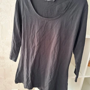 Svart topp med trekvartsärm från Still strl: XL - En enkel svart topp från Still i storlek XL. Modellen har rund halsringning och trekvartsärm, vilket ger en avslappnad men ändå stilren look. Tillverkad i mjuk bomull som känns skön mot huden. Perfekt att matcha med jeans eller kjol för en clean vibe.