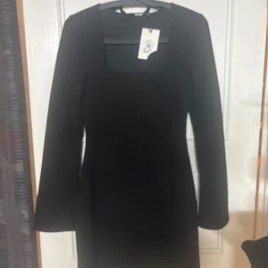 Svart långärmad klänning med fyrkantig ringning - Stilren svart klänning från NA-KD med lång ärm och snygg fyrkantig ringning. Klänningen har en figurnära passform och är perfekt för dig som gillar minimalistisk och trendig stil.