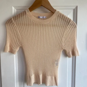 Beige ribbad topp från Zara - Supersöt beige ribbad topp från Zara med korta ärmar och rund hals. Toppen är stickad i ett lätt och luftigt material med transparenta partier upptill och har en figurnära passform. Perfekt för dig som gillar en stilren och trendig look.