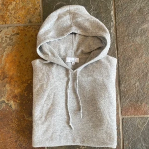 Grå Kashmir hoodie - Mysig grå hoodie från Carmes i storlek M. Tröjan har huva med snörning och är tillverkad i 100% Kashmir , perfekt för chill dagar. Enkel och stilren design som funkar till det mesta.
