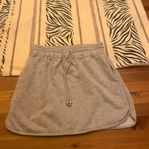 Grå mjukis-kjol från Bik Bok Balance - Supermjuk grå kortkjol från Bik Bok Balance i sweatshirtmaterial. Kjolen har elastisk midja med dragsko och två fickor i sidorna. Perfekt för chill dagar eller när du vill vara bekväm men ändå snygg.