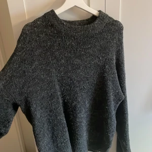 Mörkgrå stickad tröja från 157 - Mysig mörkgrå stickad tröja från 157 med rund halsringning och lång ärm. Den ser väldigt nopprig ut på bilderna men det är den inte 