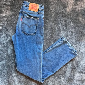 Levi's Jeans 501 - Klassiska blå Levi's 501 jeans med raka ben och normal passform. Jeansen har fem fickor, knappgylf och den ikoniska läderpatchen bak i midjan. Tillverkade i slitstarkt denim med snygga slitningar för en cool look.