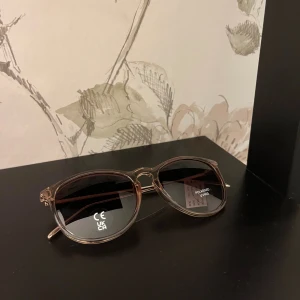 Rosa solglasögon från Pilgrim - Snygga solglasögon från Pilgrim med rundad form och transparent rosa båge. Glasen är mörka och polariserade med UV400-skydd. Metallbågarna har en stilren, tunn design och medföljer ett brunt fodral med Pilgrim-logga. Perfekt för soliga dagar. Nypris 499kr