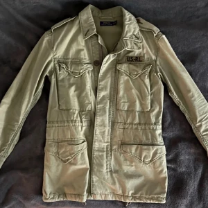 Polo Ralph Lauren Field Jacket - Säljer en beige fieldjacket från Polo Ralph Lauren . Jackan har flera stora fickor men en klassisk krage. Perfekt nu till hösten. Storlek XS men passar 175-183. Är själv 183 och den sitter perfekt, man kan även anpassa storleken. Skriv ett dm vid frågor 🙌😊