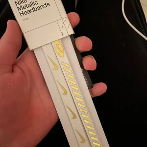 Nike Metallic diadem 3-pack vit/guld - Nike Metallic diadem i 3-pack, vita med guldiga detaljer och Nike-logga. Snygga och smala hårband som håller håret på plats under träning eller vardag. Elastiskt material för skön passform och stilren look. Använde en av 3 och säljer för billigt därav