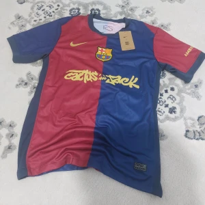FC Barcelona x Nike fotbollströja travis scott M  - Säljer en FC Barcelona x Nike fotbollströja i storlek travis scott M. Tröjan har klassisk halva-halva design i rött och blått med gula detaljer, klubbmärke och tryck på bröstet. Tillverkad i Dri-FIT material som andas, perfekt för match eller träning.