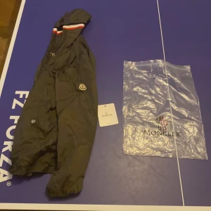 Svart vindjacka från Moncler med huva - Hej säljer min moncler jacka, den är inte använd alls mycket. Säljer för den e lite för stor för mig men den är riktigt snygg och har scan i loggon och indtrics taggs, ni kan lista ut varför den säljs billigt