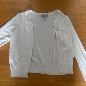 Vit kofta från H&M i bomull XS - Säljer en klassisk vit kofta från H&M i storlek XS. Koftan har långa ärmar, rund halsringning och knäppning framtill med små knappar. Tillverkad i mjuk bomull och passar perfekt till lager-på-lager-stil.