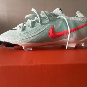 Nike Phantom GX PRO (Flyknit) fotbollsskor mintgrön - Säljer ett par Nike Phantom GX PRO fotbollsskor MED Flyknit i mintgrönt med en snygg röd swoosh på sidan. Skorna har snörning, platt sula med dobbar och är tillverkade i lätt syntetmaterial för bästa känsla på planen. Perfekta för dig som vill sticka ut på matchen.