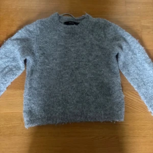 Grå stickad tröja från Vero Moda - Mysig grå stickad tröja från Vero Moda i storlek S. Tröjan har en klassisk rund halsringning och långa ärmar. Perfekt för kyliga dagar och enkel att matcha med jeans eller kjol.
