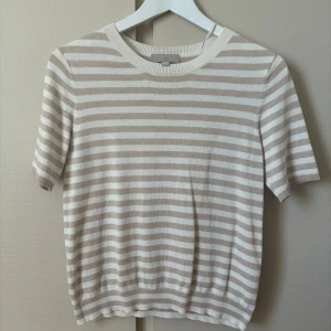 Randig kortärmad tröja från Hm - Beige och vit randig tröja från Hm. Tröjan är stickad i mjuk bomull och har en klassisk, avslappnad passform.