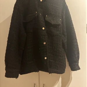 Svart overshirt från Zara - Säljer en svart jacka från Zara med grov textur och två stora bröstfickor. Jackan har guldiga knappar. 