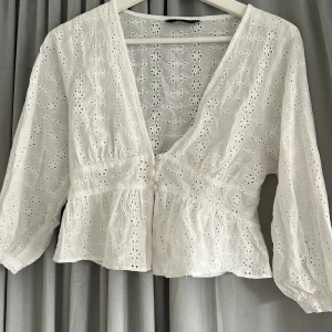 Vit broderad blus från Zara - Superfin vit blus från Zara med broderade blommor och v-ringning. Blusen har knappar framtill, volang nedtill och trekvartsärmar. Perfekt för vår och sommar, i luftig bomull som känns lätt och fräsch. Säljer då den är för liten🥰