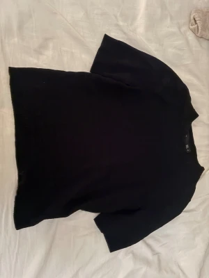 Svart stickad polotopp från 157 XS - Svart stickad polotopp från 157 i storlek XS. Toppens design är enkel med korta ärmar och en högre hals, vilket ger en clean och stilren look. Materialet är mjukt och stickat, perfekt för att skapa en chill vibe. Snygg att matcha med jeans eller kjol.